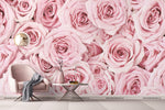 A modern room with a large Decor2Go Wallpaper Mural Pink Paradise Wallpaper Mural featuring pink roses, a pink armchair, a small white table with a book and glasses, and a decorative twig. A white floor complements.