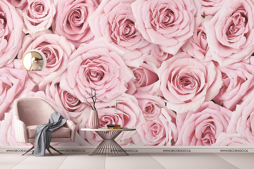 A modern room with a large Decor2Go Wallpaper Mural Pink Paradise Wallpaper Mural featuring pink roses, a pink armchair, a small white table with a book and glasses, and a decorative twig. A white floor complements.