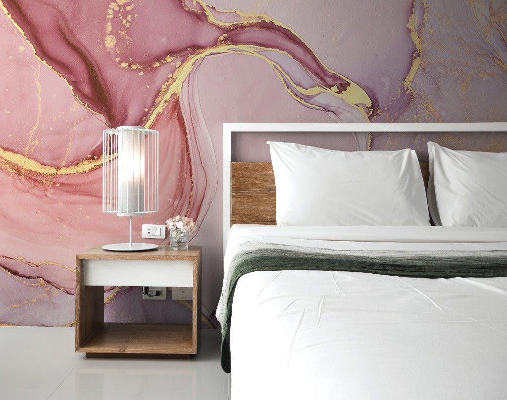 A stylish bedroom with a large bed featuring white bedding and a wooden headboard, a small wooden bedside table with a modern lamp, and a vivid Decor2Go Pink and Gold Marble Wallpaper Mural in the background.