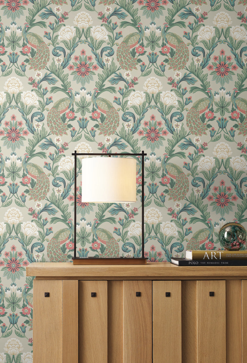 A modern table lamp with a rectangular shade sits on a wooden cabinet featuring a pattern of square panels. Behind it, Plume Dynasty Peacock & Floral Wallpaper - Taupe/Multi (60 SqFt) by York Wallcoverings enhances the background. A glass orb and a book titled "ART" complement the sophisticated design found on the cabinet.