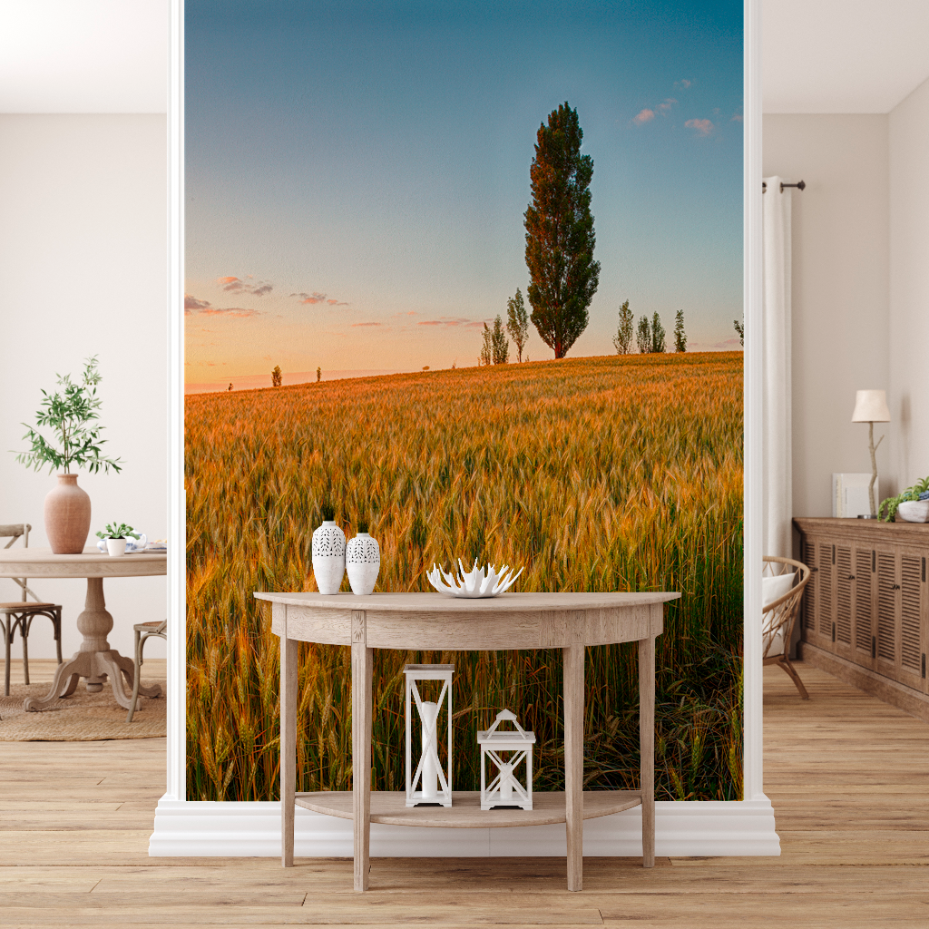 A room with minimalist decor featuring a large floor-to-ceiling Prairie Sunrise Wallpaper Mural from Decor2Go, depicting a golden wheat field at sunset with a lone tree visible in the distance. A simple wooden table and lanterns in the room complement the mural perfectly.