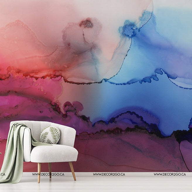 A modern room with a white armchair and a green throw over it, next to a small table with plants. The wall features a vibrant and colorful abstract painting in shades of blue, red, and Rainbow Haze Wallpaper Mural by Decor2Go Wallpaper Mural.