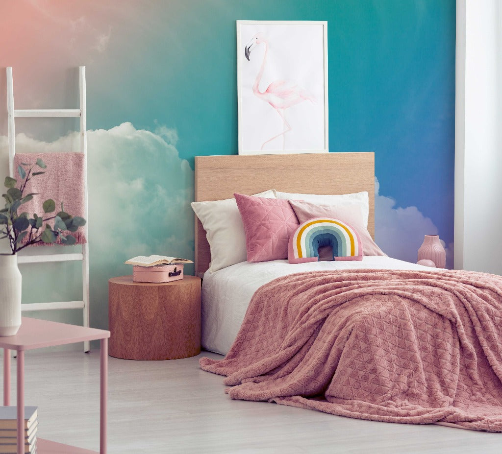 A cozy, contemporary bedroom featuring a double bed with pink bedding and a rainbow pillow, teal and pink walls adorned with a Decor2Go Rainbow Sky Wallpaper Mural, a flamingo art piece, and minimalist furniture.