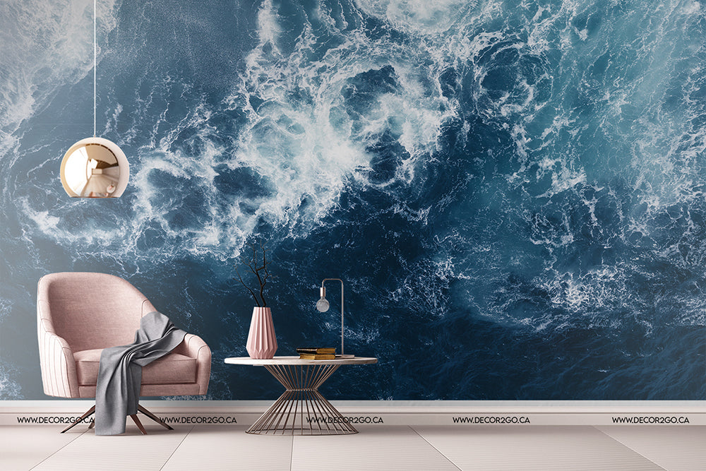 A stylish living room with a plush pink armchair and a small coffee table under a hanging lamp, against a Decor2Go Wallpaper Mural of Realm of Poseidon swirling ocean waves.