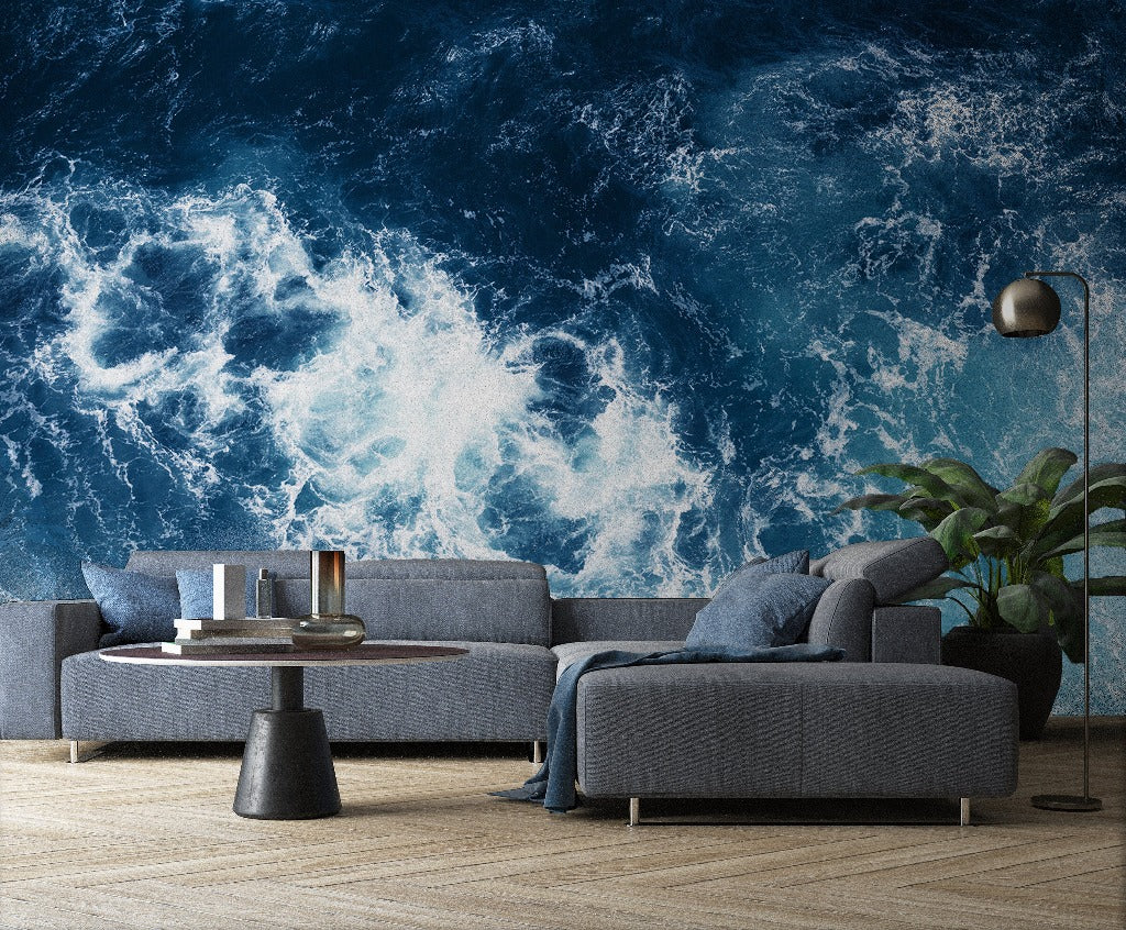 A modern living room featuring a blue sofa set against a vibrant Decor2Go Realm of Poseidon Wallpaper Mural of ocean waves, accompanied by a black floor lamp, round table, and indoor plant.