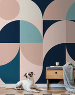 A dog lying on a rug against a backdrop of a Decor2Go Wallpaper Mural in shades of navy, teal, and peach. Next to the dog is a small wooden nightstand with a cup and a.