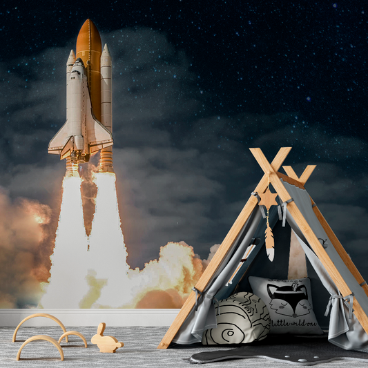 A digital composite image with a Rocket to the Moon Wallpaper Mural by Decor2Go Wallpaper Mural in the background and a child's play area featuring a teepee, plush cushions, and wooden toys in the foreground under a starry sky.