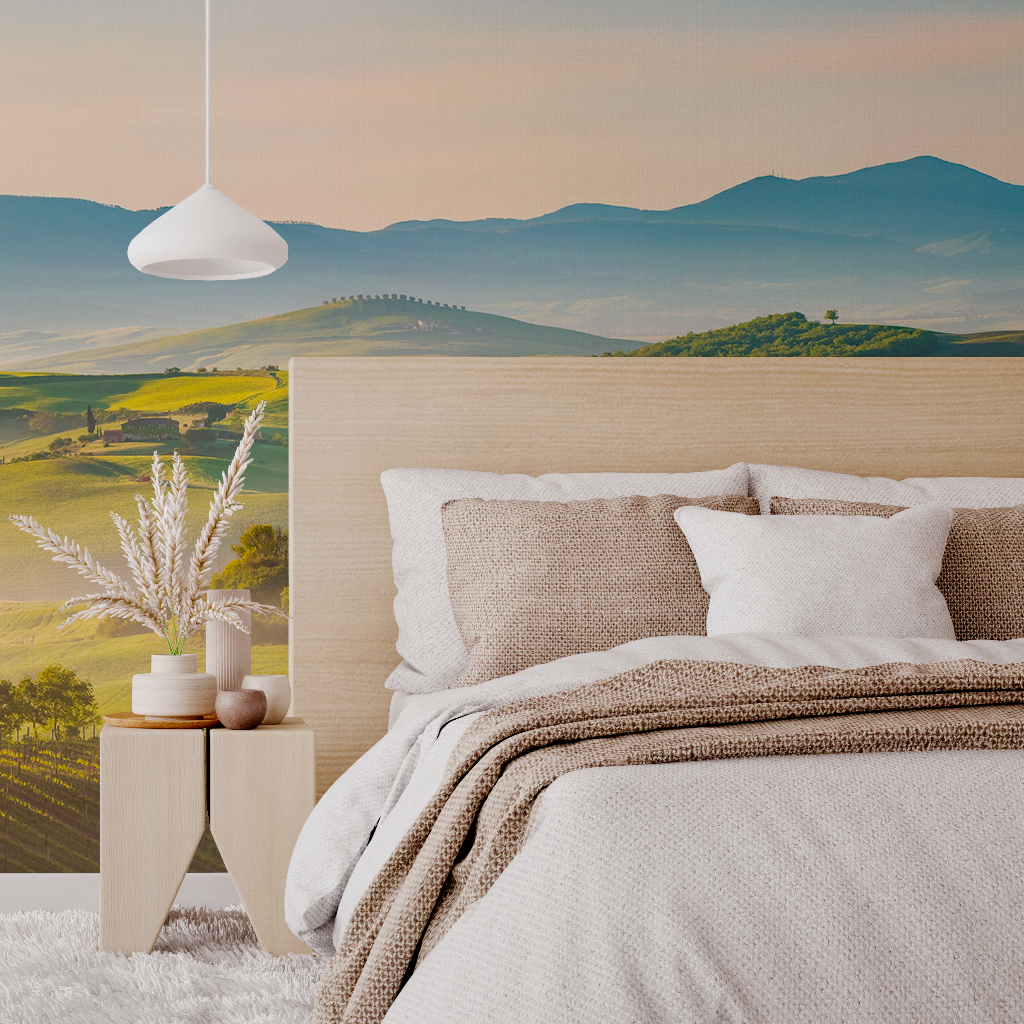 Bedroom - A cozy bedroom featuring a bed with neutral-toned bedding and multiple pillows, beside a wooden nightstand with decorative plants. A large Decor2Go Wallpaper Mural of Rolling Hills adds a tranquil backdrop.