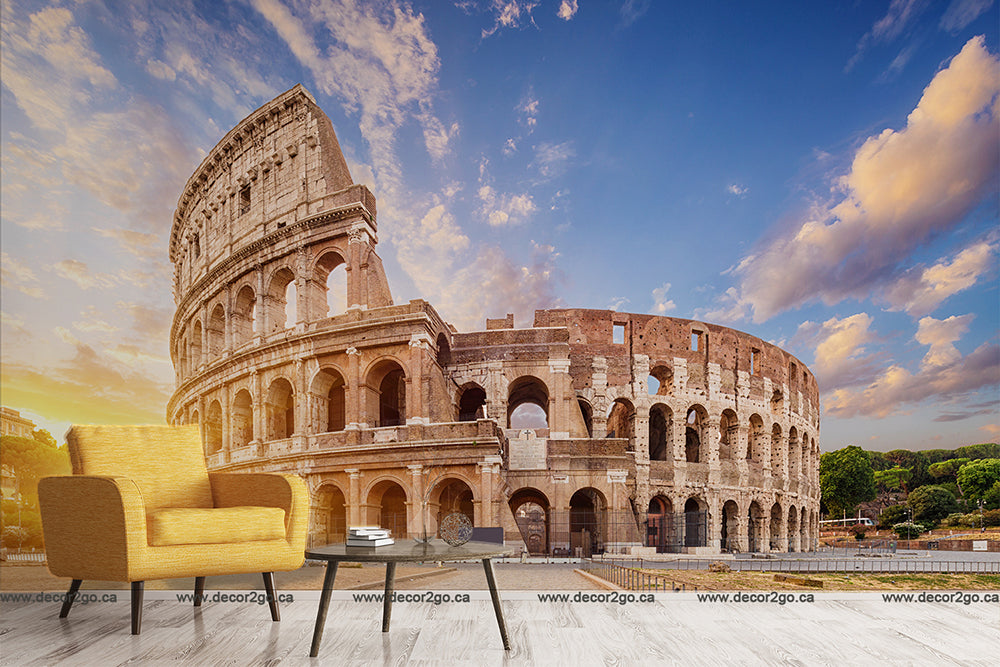 A surreal image combining a modern living room set, featuring a yellow armchair and glass coffee table, with the Decor2Go Wallpaper Mural Roman Colosseum Wallpaper Mural in the background under a blue sky.
