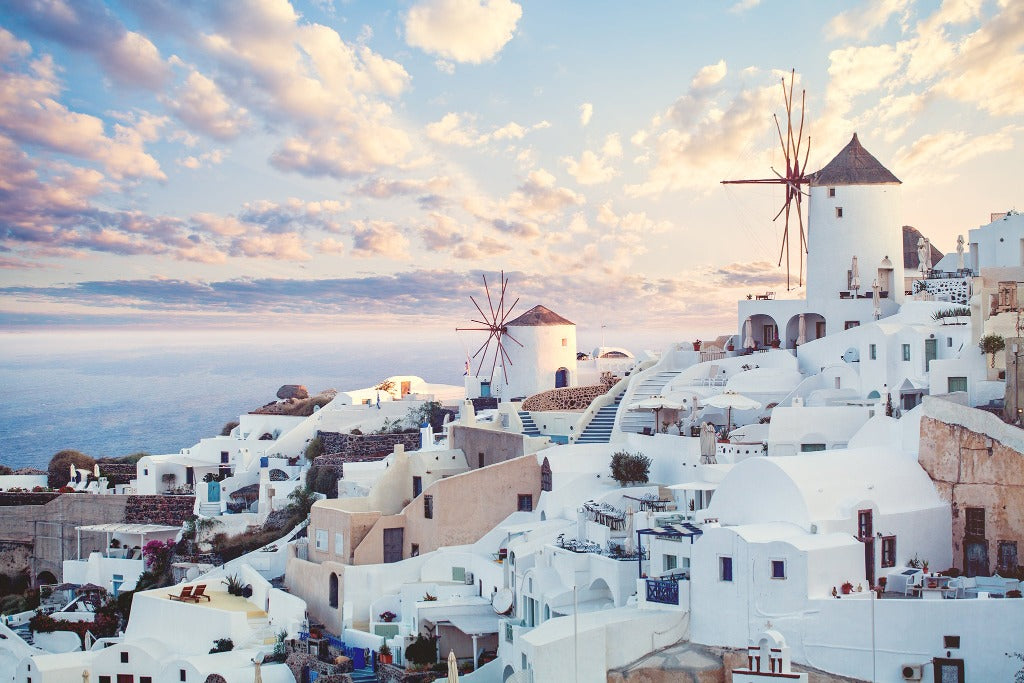 Panoramic view of the Santorini Skyline Wallpaper Mural by Decor2Go Wallpaper Mural, Greece, showing white buildings and windmills against a sunset sky with the Aegean Sea in the background.