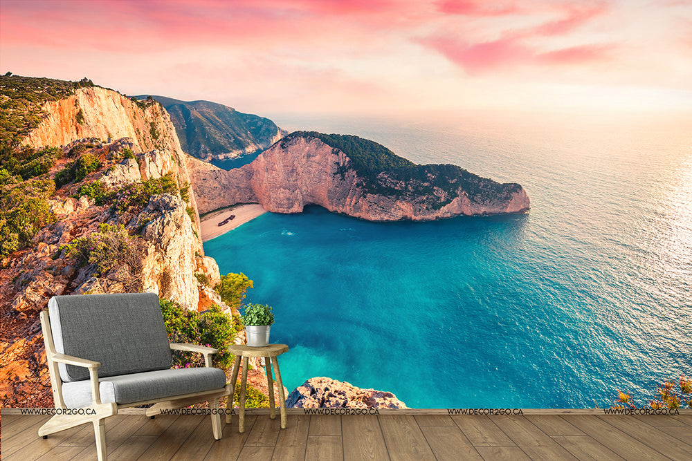 A serene digital composite image of an armchair and side table on a wooden platform overlooking a breathtaking coastal view with steep cliffs and a turquoise sea under a Decor2Go Wallpaper Mural sky.