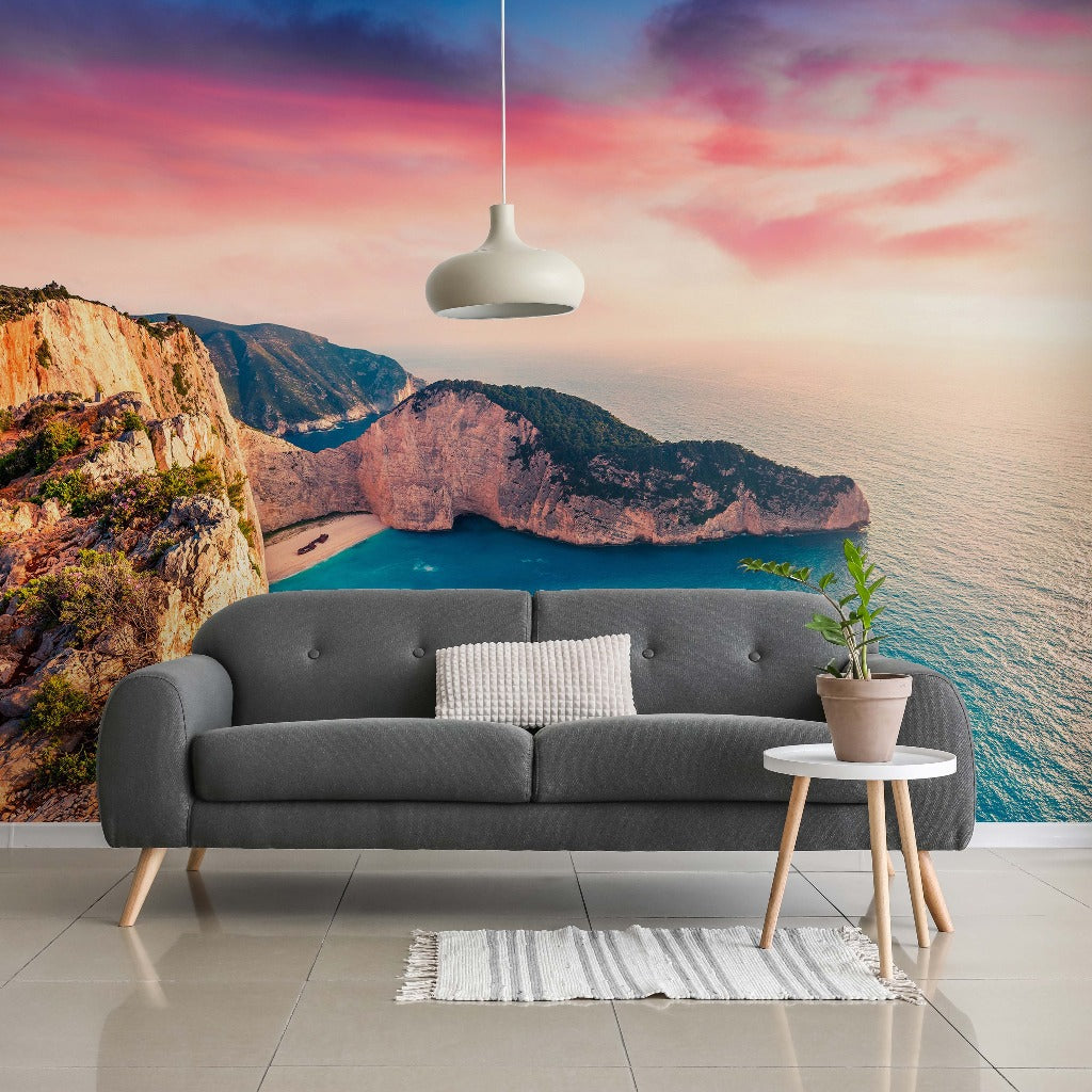 A modern living room with a gray sofa, white rug, and small wooden table, set against a large floor-to-ceiling feature wall of a dramatic Sea Horizon Wallpaper Mural by Decor2Go Wallpaper Mural at sunset.