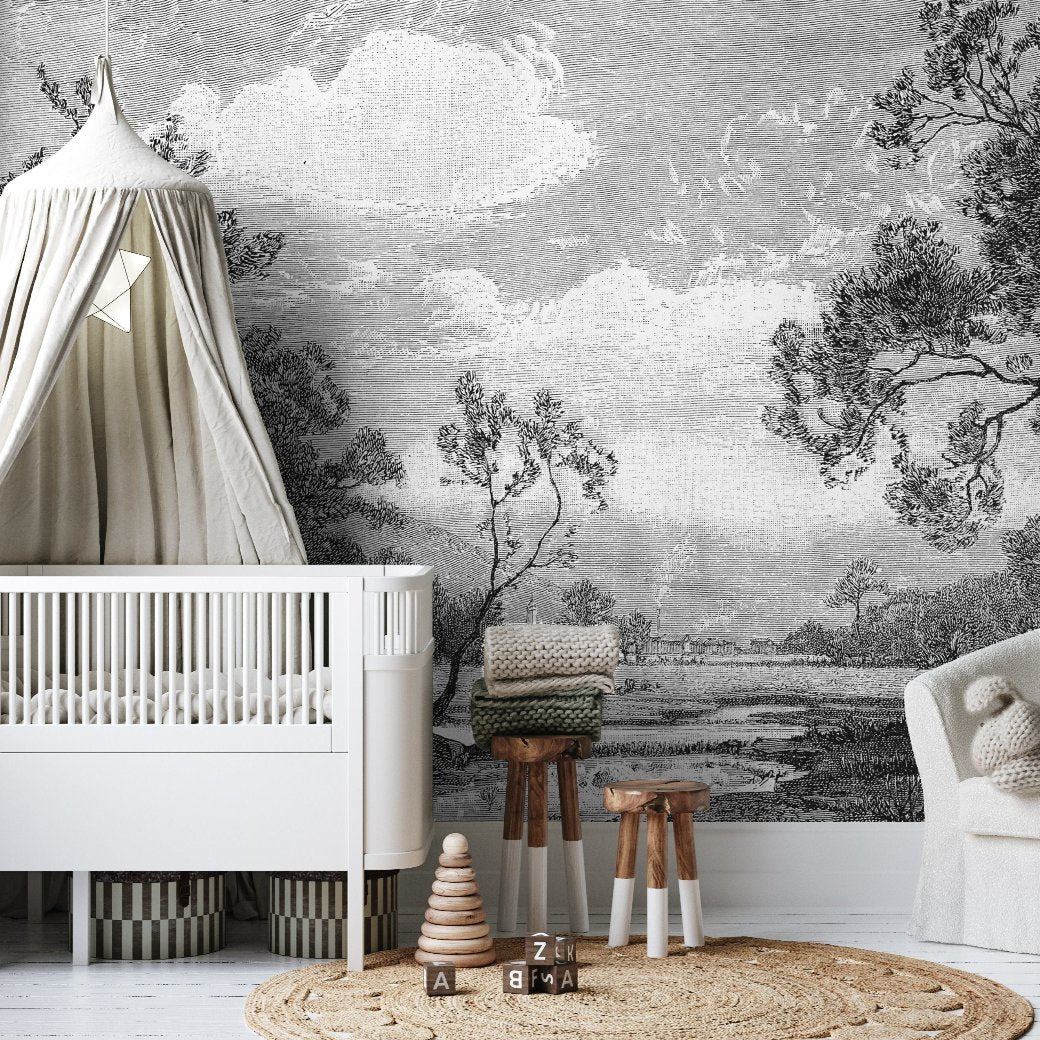 A nursery exuding timeless vintage elegance is adorned with a white crib and a canopy, complemented by the Decor2Go "Serene Forest Wallpaper Mural," which depicts a tranquil black and white landscape. A cozy armchair, wooden stool, woven baskets, and toys contribute warmth to the peaceful setting.