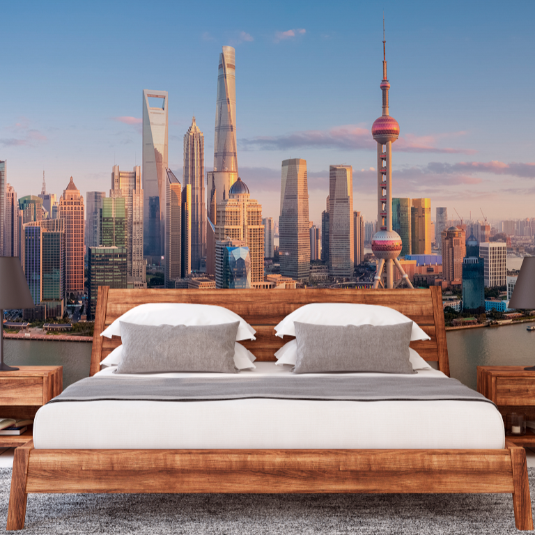 A modern bedroom featuring a wooden bed with white bedding and two bedside tables, set against a large Decor2Go Wallpaper Mural of the Shanghai Skyline at sunset.