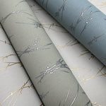 Three rolls of York Wallcoverings' Smokey Blue & Silver Sprigs Wallpaper cover 60 SqFt, showcasing nature-inspired branches and leaves in smokey blue fleece, gray, and beige with silver metallic accents. It has a matte texture with a subtle sheen.