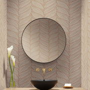 Bathroom - A modern has a round mirror with a black rim against York Wallcoverings' Blush & Gold Luminous Leaves Wallpaper. Below is a black basin with gold faucets from the modern metals collection, completed by a vase with two white flowers and a soap dish