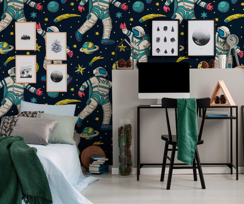 A vibrant bedroom-office with Decor2Go Wallpaper Mural featuring astronauts and planets. A desk with a computer, a cozy bed with green blankets, and framed artwork on the wall.