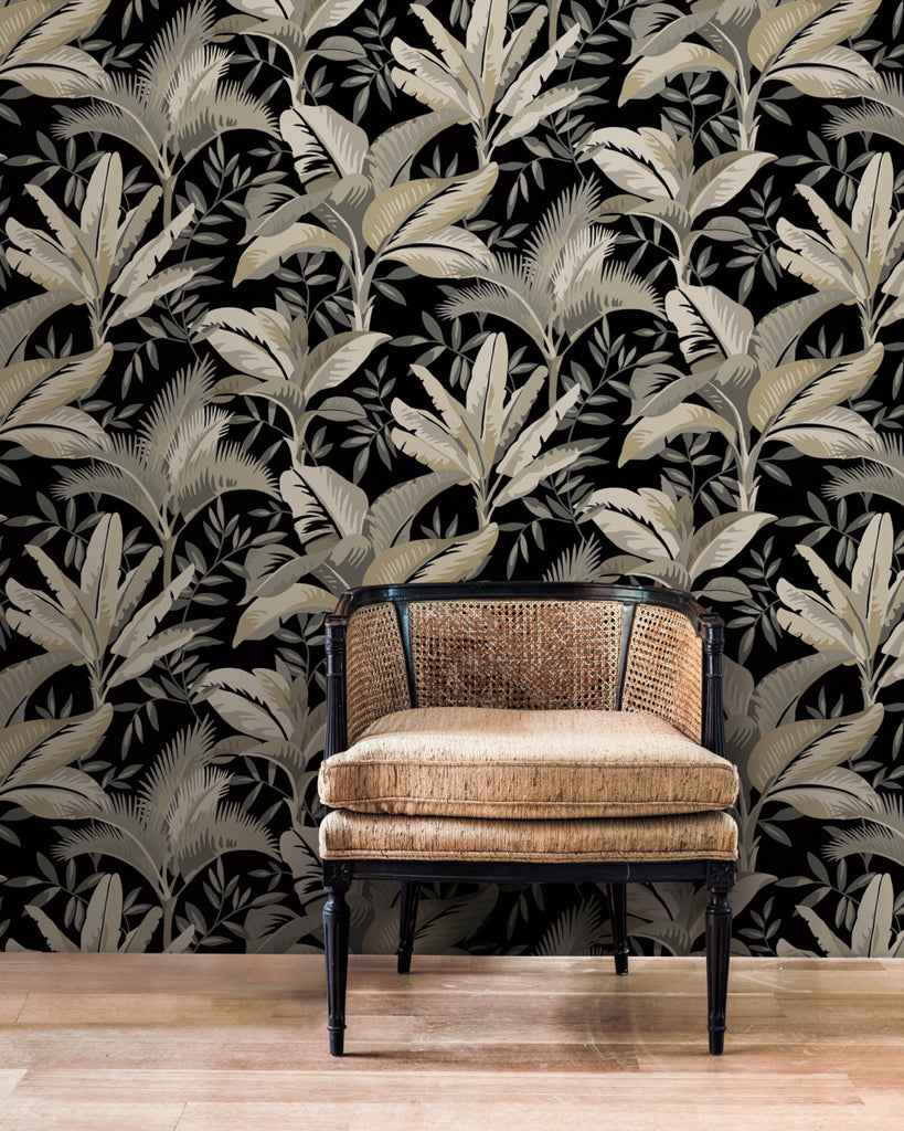 A stylish vintage chair with a rattan backrest and cushioned seat against bold York Wallcoverings Summerhouse Midnight Wallpaper in shades of black, gray, and white.