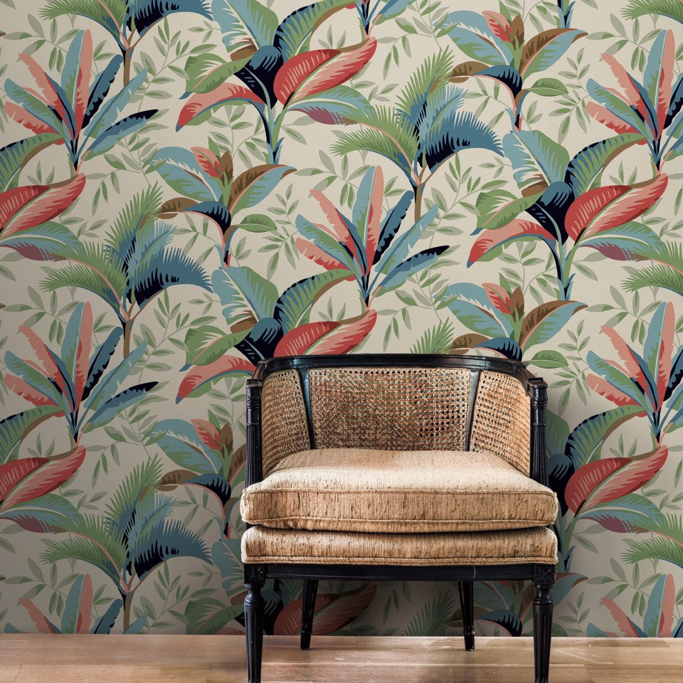 A vintage wooden bench with a wicker backrest and cushion sits against a wall covered in vibrant, Summerhouse Midnight Wallpaper Orange, Green (60 Sq.Ft.) featuring large green leaves and bright blue and red birds from York Wallcoverings.
