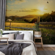 Bedroom - A cozy bedroom with a large Decor2Go Wallpaper Mural of a sunset over a scenic grassy hill with a small farmhouse, featuring a bed with gray and white bedding, and a small table with a vase of