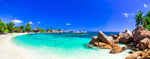 Panoramic view of a Decor2Go Wallpaper Mural destination with clear turquoise water, white sand, large rocks, palm trees, and a small hut under a blue sky.