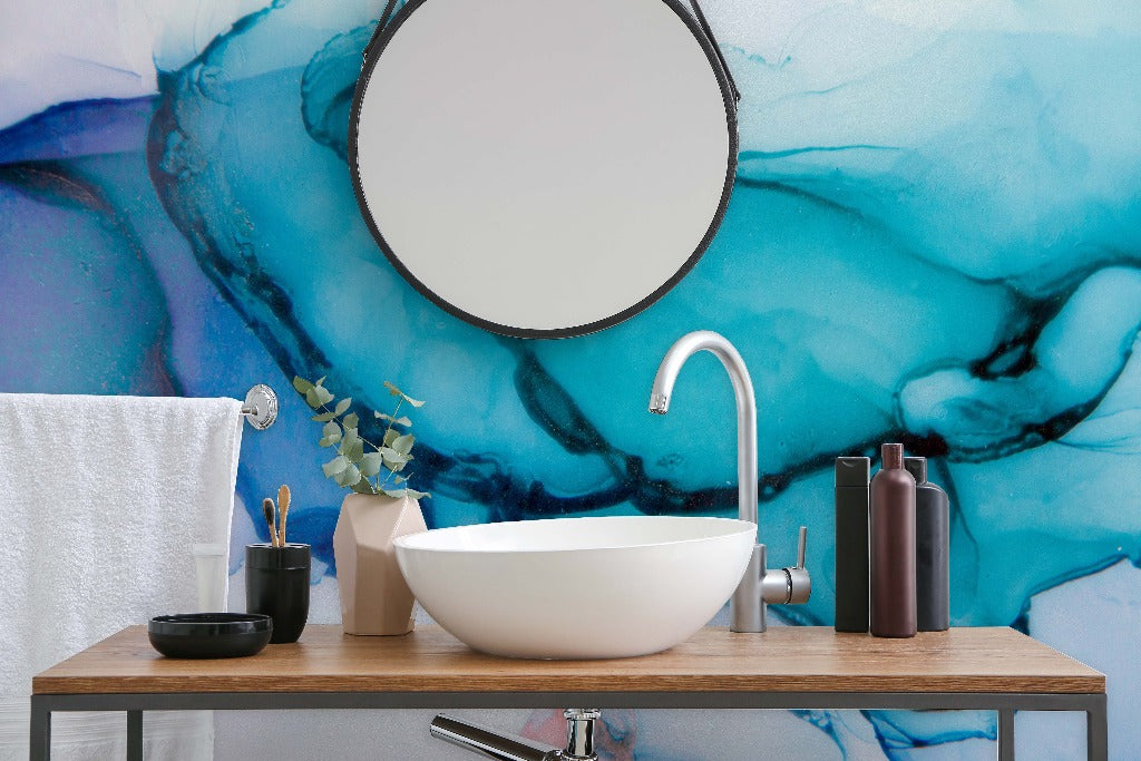 Modern bathroom vanity with a circular mirror and a vessel sink set against a Decor2Go Wallpaper Mural. Accessories include dark bottles and a plant.
