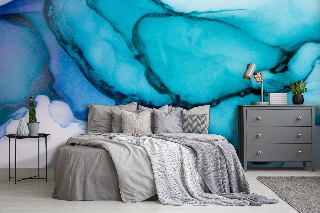 A stylish bedroom featuring an oversized Decor2Go Turquoise Ink Wallpaper Mural behind a bed dressed in gray linen. Beside the bed is a dark gray dresser and a small table with a plant and lamp.