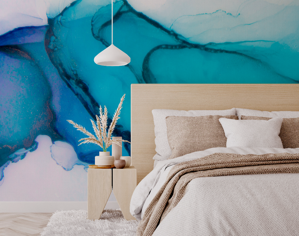 A modern bedroom featuring a king-sized bed with beige linens against a vibrant deep blue and Decor2Go Wallpaper Mural. A minimalist side table holds plants and books, complemented by a hanging white lamp.