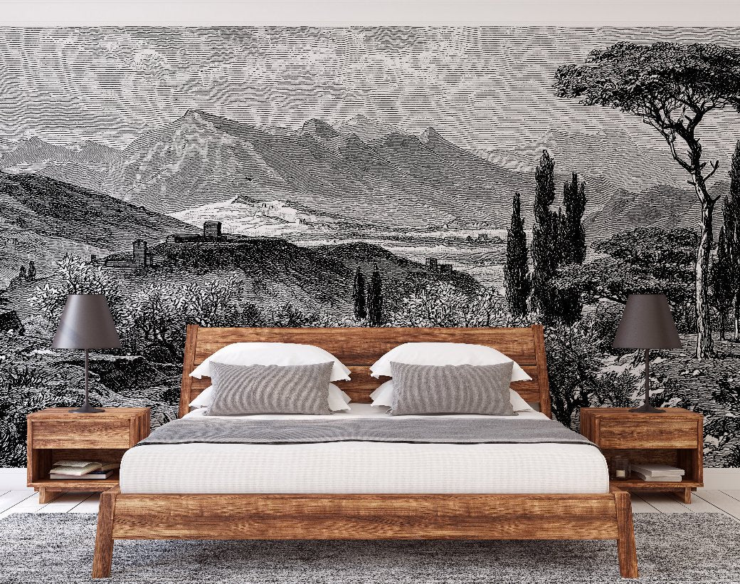 A bedroom featuring a rustic wooden bedframe paired with two matching nightstands showcases white linens and striped gray pillows on the bed. Each nightstand hosts a gray table lamp. The wall behind is adorned with Decor2Go Wallpaper Mural's Tuscan Serenity, which depicts a black and white mountain landscape.