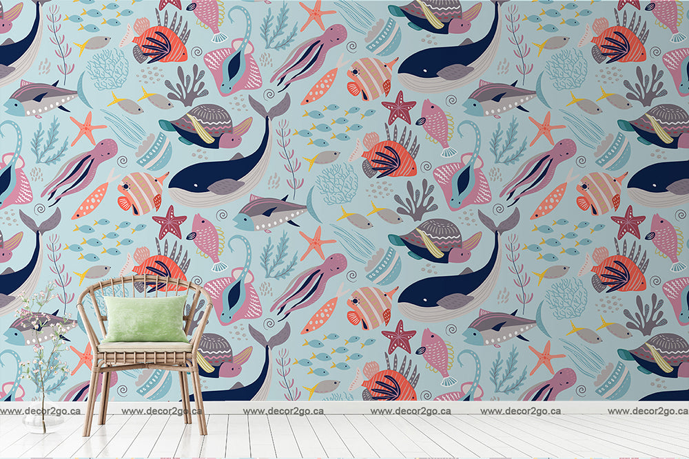 A child's room with a vivid Decor2Go Wallpaper Mural featuring whales, fish, and squid in pastel colors. A rattan chair with a green cushion is placed against the wall.