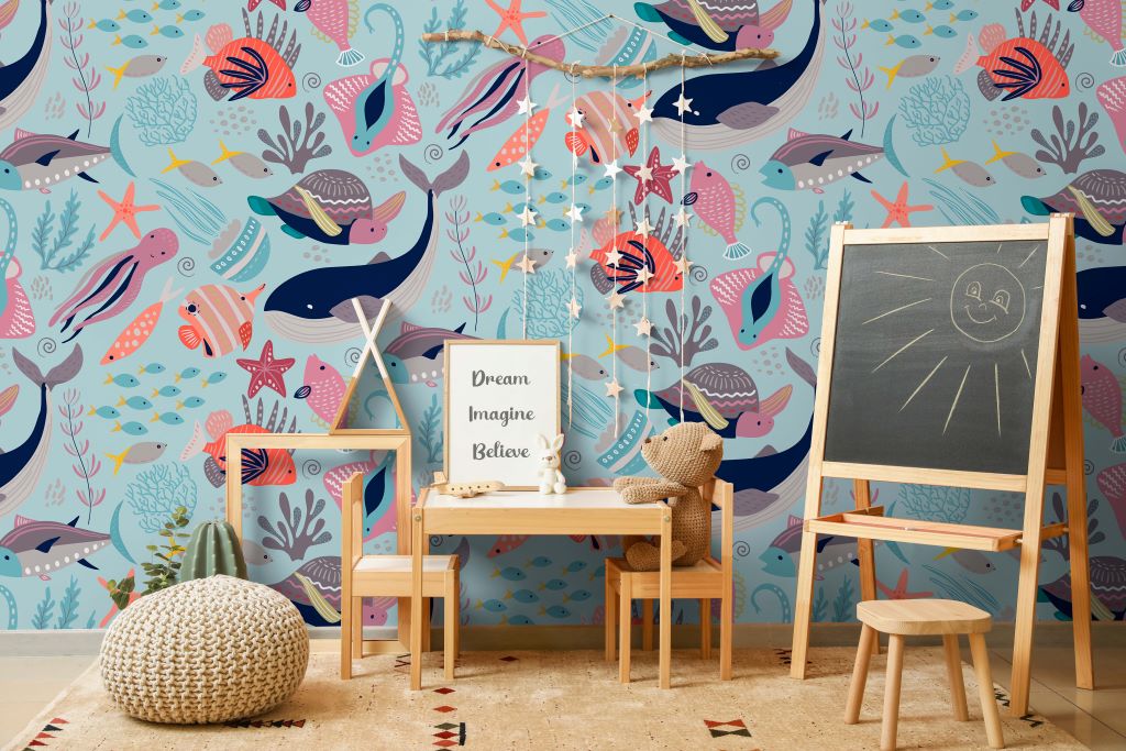 A colorful children's playroom with Decor2Go Wallpaper Mural, featuring multiple fish and whales. There's a small wooden desk with a "dream, imagine, believe" sign, a chalkboard, and