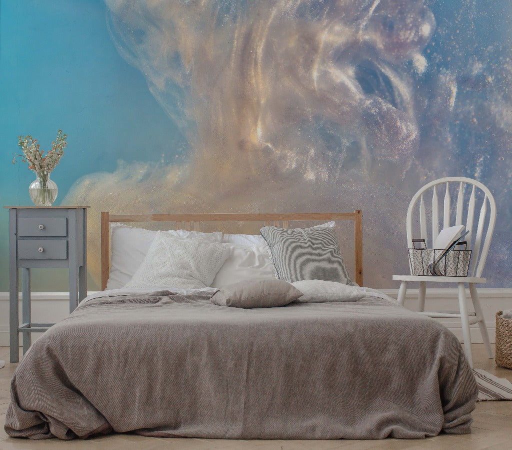A cozy bedroom with a double bed covered in gray linen, set against a striking Decor2Go Wallpaper Mural of a galaxy. A white chair and a grey nightstand with a vase and books complete the serene ambiance.