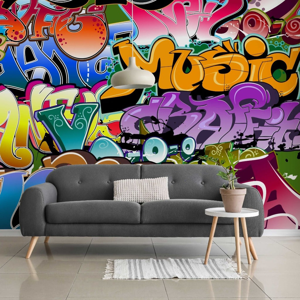 A vibrant living room with a wall covered in colorful Urban Colors Wallpaper Mural featuring various shapes and the word "music". A modern grey sofa with a pillow, a small white side table, and a potted