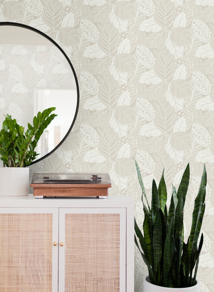 A stylish room corner featuring a white cabinet with cane webbing and a round mirror, a record player, a potted snake plant, and a small plant on the cabinet, against durable York Wallcoverings Vinca Eucalyptus Wallpaper Green (60 Sq.Ft.).