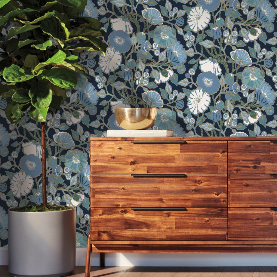 black blue floral wallpaper on the wall, wooden dresser in front of the wall and big green plant