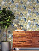 yellow blue floral wallpaper on the wall, wooden dresser in front of the wall and big green plant