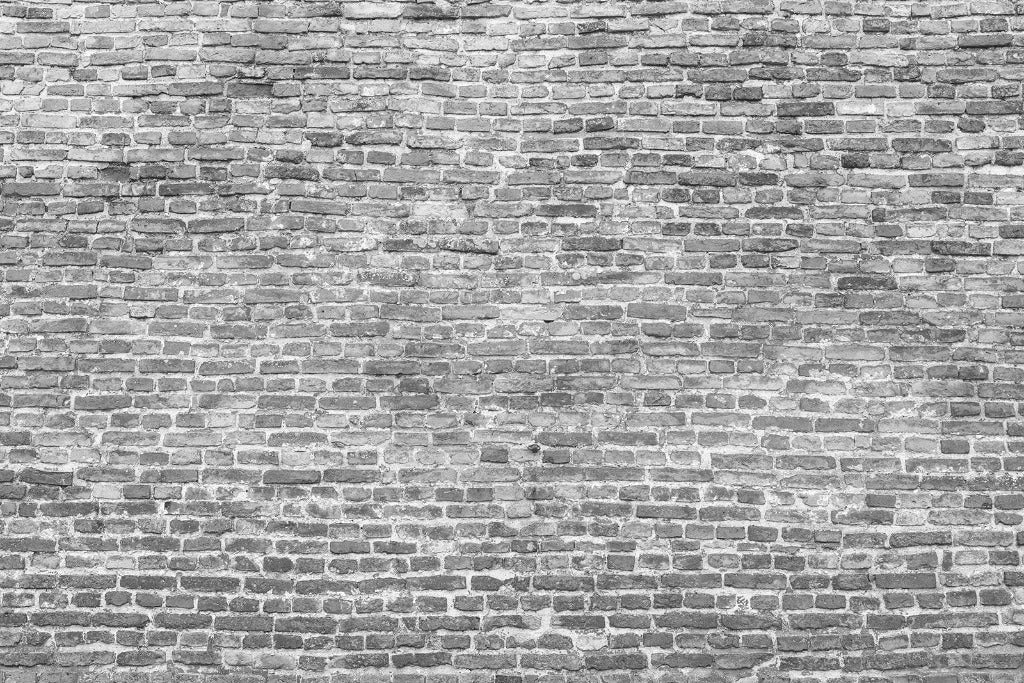 A black and white photograph of a Washed Grey Brick Wall Wallpaper Mural. The bricks vary slightly in size, and the wall has a rough, uneven texture with visible mortar lines. The overall appearance shows weathering and age, contributing to its modern elegance and industrial-chic aesthetic. This mural is from Decor2Go Wallpaper Mural.
