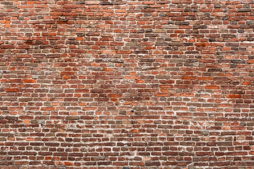 A close-up view of an old brick wall, showcasing a variety of red and brown bricks. The wall exudes rustic elegance with its uneven, weathered texture, darker patches, and white mortar lines in between the bricks—an ideal choice for the Decor2Go Wallpaper Mural Washed Classic Brick Wall Wallpaper Mural to enhance versatile decor.