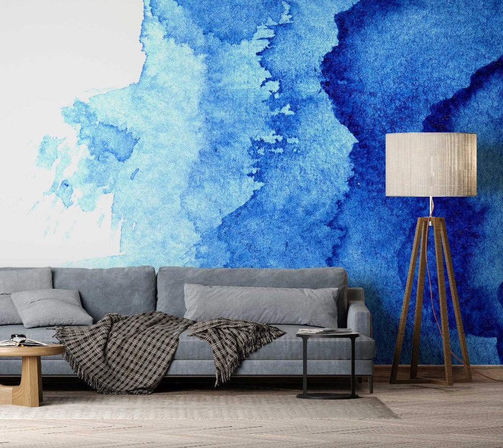 A modern living room featuring a gray sofa with cushions and a checkered throw blanket, beside a tall wooden floor lamp, against a vibrant Waterblue Ink Wallpaper Mural, by Decor2Go Wallpaper Mural.