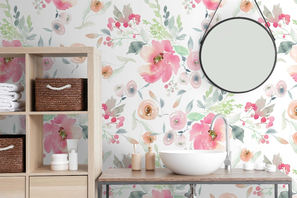 A serene bathroom with Watercolor Pink Flowers Wallpaper Mural from Decor2Go Wallpaper Mural in pink and green tones, a round mirror above a white sink, wooden shelving with towels and toiletries, and decorative candles.