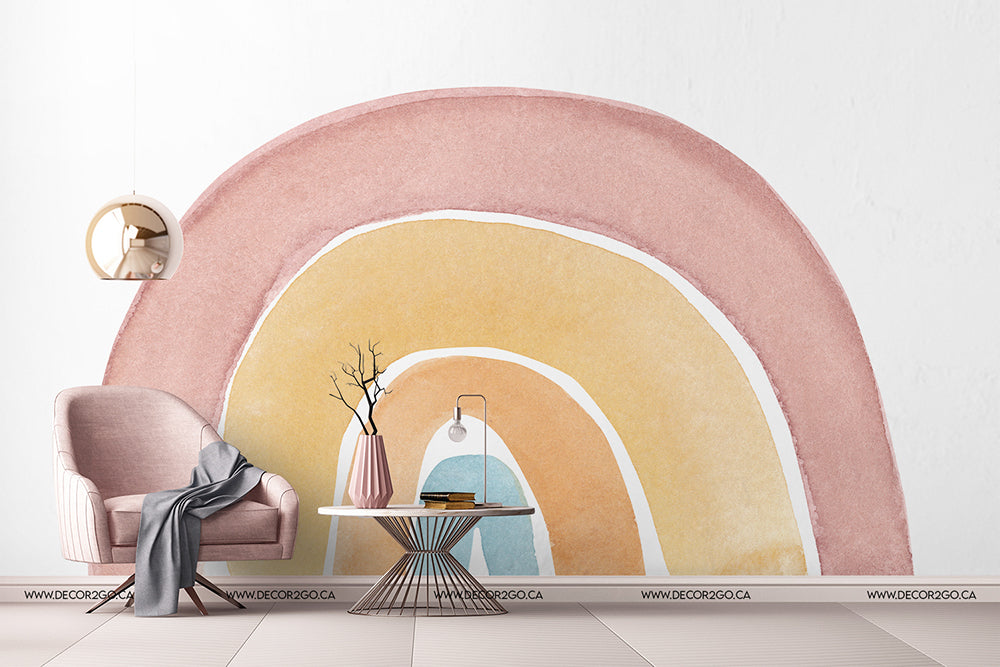 Kids Room - A stylish children's room corner with a Watercolor rainbow Wallpaper Mural arch by Decor2Go Wallpaper Mural, featuring a plush pink armchair, a gray throw blanket, a round side table with a vase and books, and a modern hanging