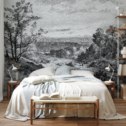 A bedroom showcasing a spacious bed adorned with white and blue blankets is accompanied by wooden nightstands with lamps. The wall behind the bed features the "Whispering Trees Wallpaper Mural" by Decor2Go, capturing nature's tranquil charm in black and white. To the right, a cozy bookshelf completes the ambiance.