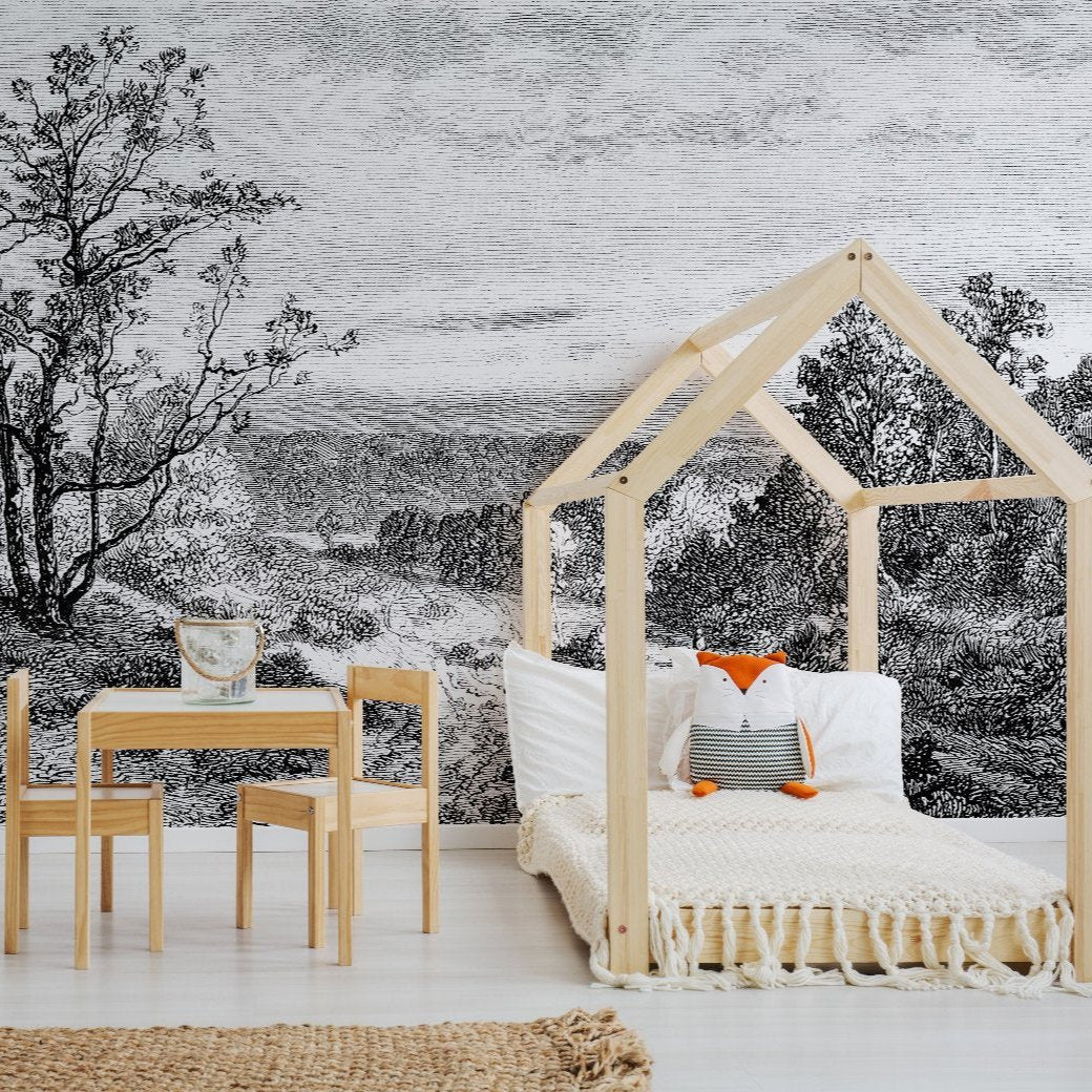 A child's room features a wooden house-shaped bed and a table with chairs. A fox plush toy and cushions are on the bed, while the wall showcases the Whispering Trees Wallpaper Mural from Decor2Go, depicting whispering trees in a serene landscape. A woven rug lies on the light wooden floor.