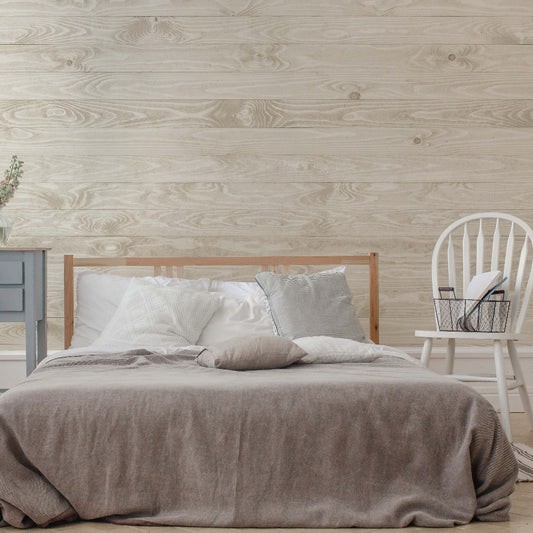 A cozy bedroom featuring a neatly made bed with gray bedding, a wooden headboard, a gray nightstand, and a white chair with a book against a Decor2Go Wallpaper Mural.