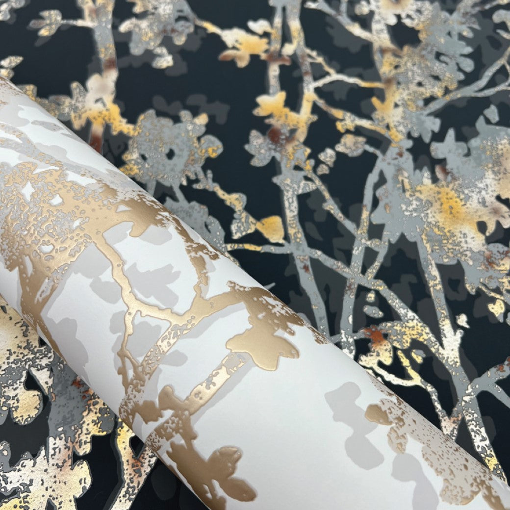 Discover York Wallcoverings' White & Gold Shimmering Foliage Wallpaper. This roll features an elegant floral pattern with luxurious metallic gold accents on a dark background, creating delicate branches and leaves to enhance any sophisticated space.