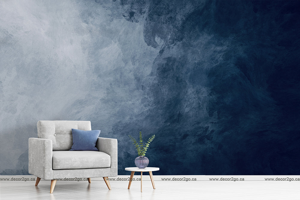 A minimalist living room with a grey armchair, a navy blue cushion, a small round table with a plant, against an abstract Decor2Go Wallpaper Mural feature wall.