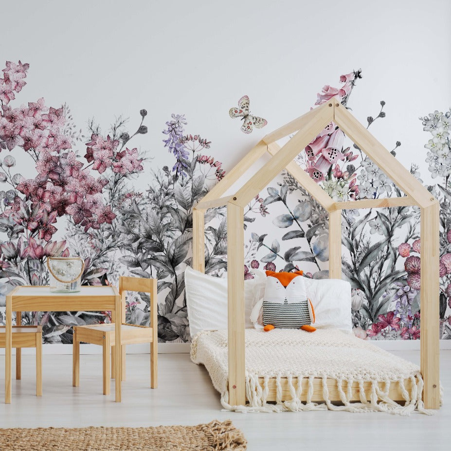 A cozy children's bedroom with a wooden house-shaped bed frame, colorful pillows, and a small wooden table with chairs. The room is decorated with Decor2Go Wallpaper Mural featuring Wild Flower designs.
