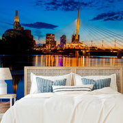 Bedroom - A luxurious bedroom with a bed facing a large window showcasing a scenic view of a "Decor2Go Wallpaper Mural," featuring the striking cable-stayed bridge and illuminated buildings reflecting on a river.