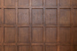 The office aesthetic is enhanced by a wooden wall featuring a grid pattern, formed by evenly spaced rectangular panels framed by narrow, rectangular indentations. The wood has a smooth finish and a rich, warm brown color, exhibiting natural grain variations and a polished surface. Decor2Go Wallpaper Mural's Wood Panels III Wallpaper Mural provides this stunning look.