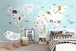 A children's bedroom features a Decor2Go Wallpaper Mural World Map with Wild Animals Blue Wallpaper Mural with animals representing different regions. The space includes a bed with polka-dot bedding, a white nightstand, a modern white chair, and framed quotes. Toy decor and a cozy ambiance complete the playful look.